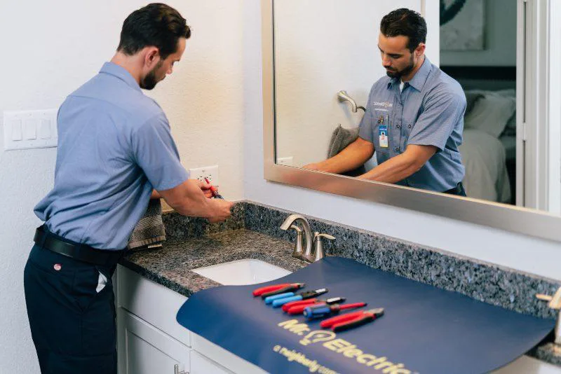 Mr. Electric technician repairing an electrical outlet in a bathroom next to the sink.