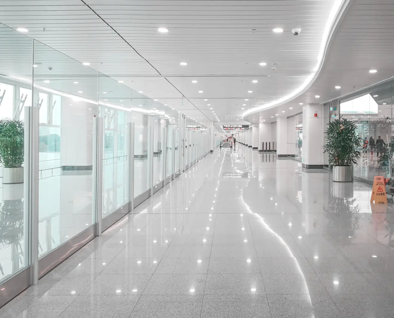 Modern commercial hallway with glossy tile flooring, glass walls, and bright energy-efficient LED lighting embedded in a curved ceiling, creating a clean and professional ambiance.