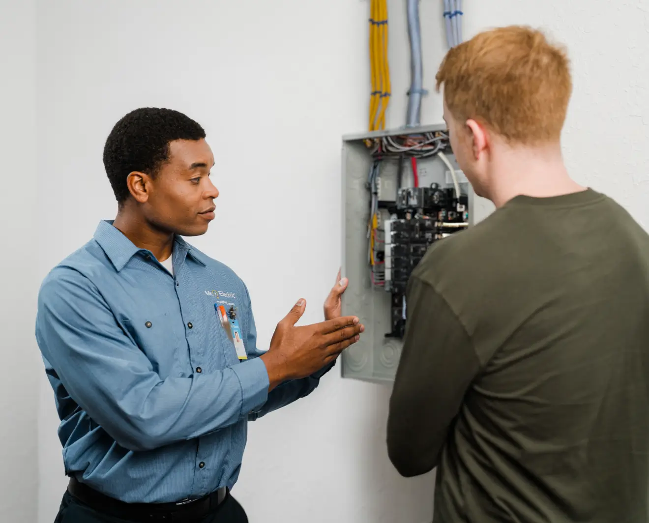 Electrician explaining the components of a residential electrical breaker panel to a homeowner during a service call.