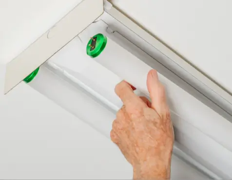 Close-up of a handyman’s hand replacing a fluorescent tube light in a ceiling fixture, focusing on proper ballast and bulb replacement for optimal lighting performance.