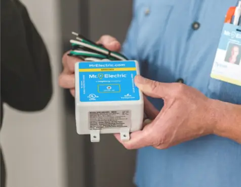 Close-up of an electrician holding a labeled Mr. Electric electrical device, wearing a blue uniform with visible name badge, symbolizing professional residential electrical services.
