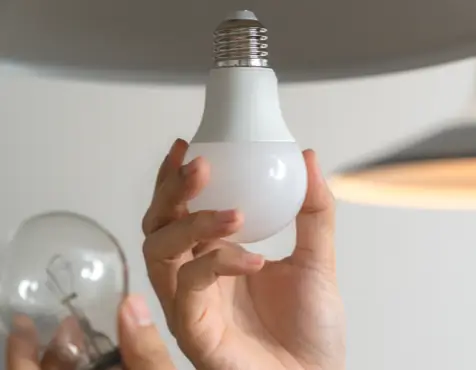 Hand replacing a traditional bulb with a modern, energy-efficient LED bulb in a light fixture, representing eco-friendly lighting solutions for the home or office.