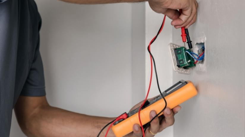 Electrician is using a digital meter to measure the voltage at the power outlet in the wall of a residential home.